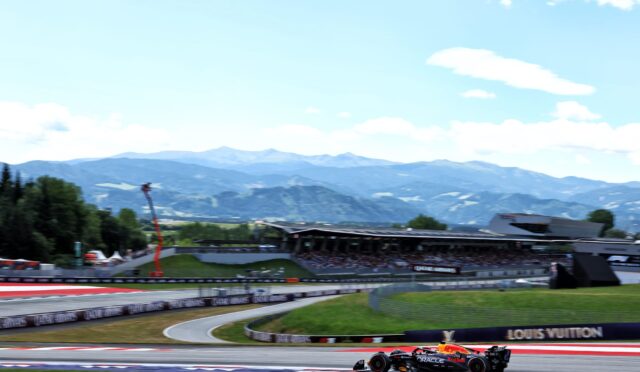 Race car with Oracle Red Bull livery speeding around a track with mountains in the background, under a blue sky.