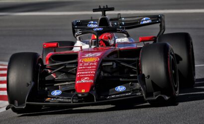 Front-facing view of a red Formula 1 race car on a track, sponsor logos visible on the body and nose cone.