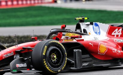 Red Formula 1 car on the track, close-up of the cockpit, front wing, and tire with sponsor logos visible.