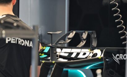 A cyclist in a dark jersey stands near high-end racing bikes mounted in a workshop setting.