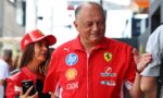 Smiling man in a red Ferrari shirt with sponsor logos, standing outdoors beside a woman in a red cap at a public event.