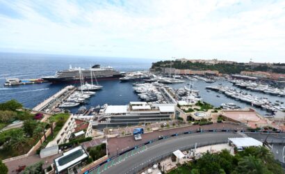 A large cruise ship docked at a busy marina surrounded by many yachts, with a hillside town in the distance.