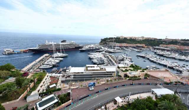 A large cruise ship docked at a busy marina surrounded by many yachts, with a hillside town in the distance.