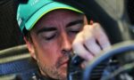 Close-up of a man wearing a teal cap with neon-green trim, eyes closed, hand near his mouth inside a vehicle cockpit