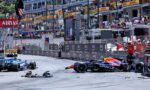 Formula 1 cars stop on a street circuit after a crash, with debris and a damaged front wing on the track and spectators watching from the barriers and grandstands behind safety fencing.