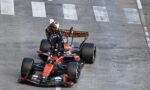 Orange Formula 1 race car with a driver in a multicolored helmet on a gray track with white lane markings visible behind the car.