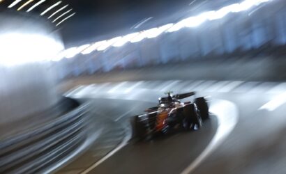 Red Formula 1 car speeding through a dim tunnel, captured with motion blur and streaks of light along the walls through a curved track.