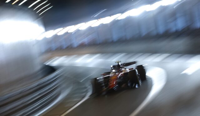 Red Formula 1 car speeding through a dim tunnel, captured with motion blur and streaks of light along the walls through a curved track.