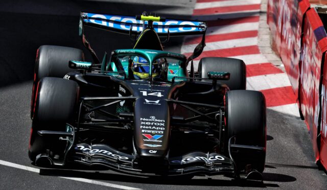 Formula One car in teal and black speeds along a race track, close to red-and-white barriers, with sponsor logos on the nose and wings nearby
