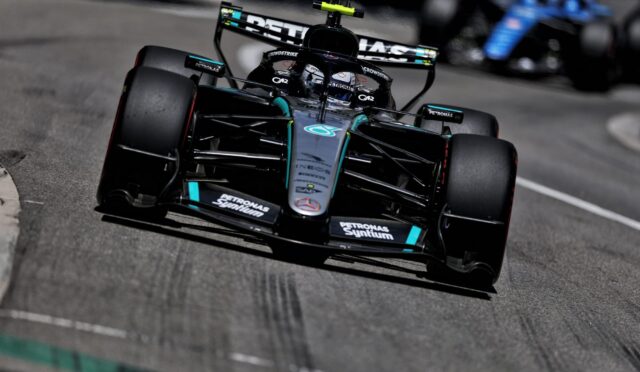 Mercedes Formula 1 car on track, close-up from the front-left, with Petronas sponsorship and rear wing visible as it speeds by.