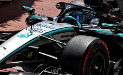Close-up of a Mercedes-AMG Formula 1 car on a brick track, showing the cockpit, front wing, and sponsor logos like Petronas and CrowdStrike on teal–silver livery.