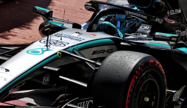 Close-up of a Mercedes-AMG Formula 1 car on a brick track, showing the cockpit, front wing, and sponsor logos like Petronas and CrowdStrike on teal–silver livery.