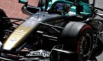 Close-up of a teal/black Formula 1 car with sponsor logos and a driver in the cockpit, tire and front wing visible.