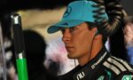 Portrait of a man in a turquoise cap with a Mercedes logo, wearing a TeamViewer racing suit and an earpiece, looking to the right.
