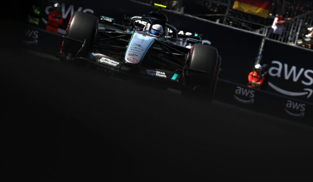 Front view of a Mercedes Formula 1 car speeding toward the camera on a dark race track, AWS branding in the background