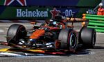 Orange McLaren Formula 1 car speeding around a corner with Heineken banners in the background.