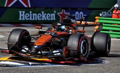 Orange McLaren Formula 1 car speeding around a corner with Heineken banners in the background.