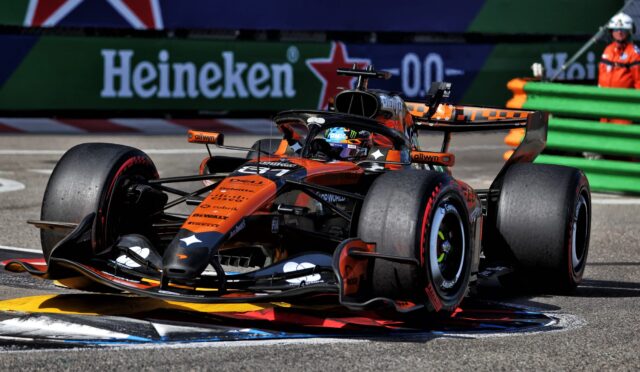 Orange McLaren Formula 1 car speeding around a corner with Heineken banners in the background.
