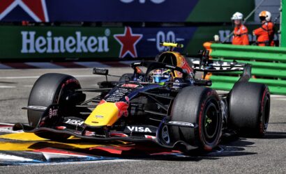 Red Bull Racing Formula 1 car on a race track near the curb, yellow nose, with Heineken ad and green barriers in the background.