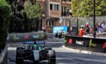 Formula 1 car in teal livery navigates a tight Monaco street circuit chicane, barriers and sponsor banners on both sides with spectators watching the action.
