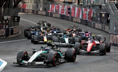 Multiple Formula 1 cars tightly packed as they race along a city street circuit, with barriers and sponsor banners lining the track.