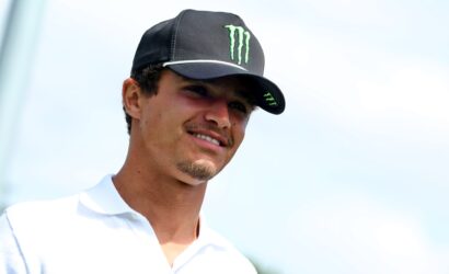 Smiling man wearing a black cap with a green Monster logo outdoors, facing right.