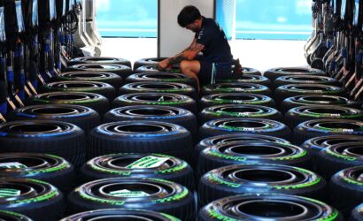 Mechanic kneeling among rows of stacked racing tires inside a trailer or transport pod.