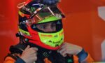 Race car driver’s neon helmet being fastened under an orange racing suit before a race.
