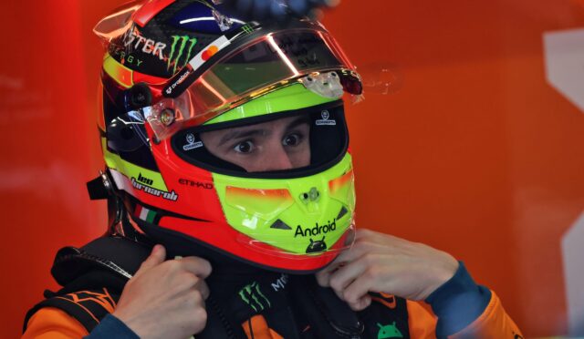 Race car driver’s neon helmet being fastened under an orange racing suit before a race.