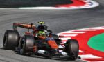 Formula 1 car negotiating a sharp turn on a race track with red-and-white curbs and green runoff area in the background