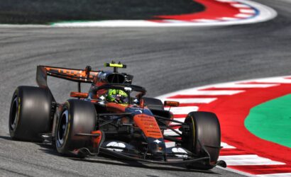 Formula 1 car negotiating a sharp turn on a race track with red-and-white curbs and green runoff area in the background