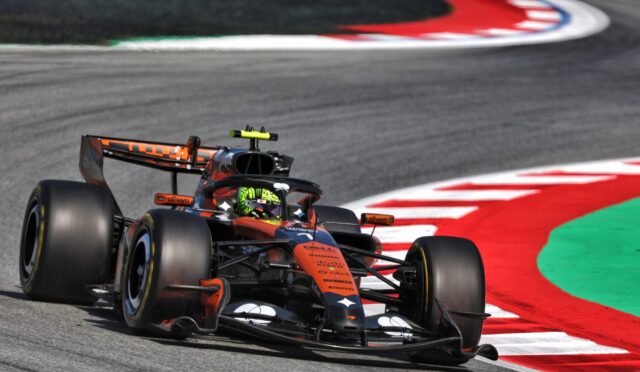 Formula 1 car negotiating a sharp turn on a race track with red-and-white curbs and green runoff area in the background