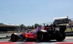 Red and pink Formula 1 car on a sunny race track with grandstands filled with spectators in the background, crossing a red curb point.