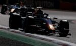 Dark photo of a Red Bull Formula 1 car in a tight bend on a race track, front wing close to the apex as others blur behind it.