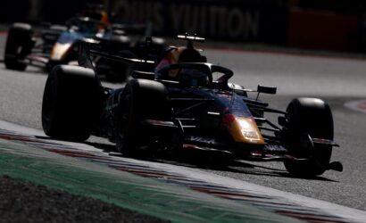 Dark photo of a Red Bull Formula 1 car in a tight bend on a race track, front wing close to the apex as others blur behind it.