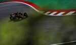 Open-wheel race car navigating a sharp curve on a racing track, with red-and-white curb and green runoff nearby.