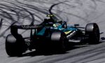 Teal and black Formula 1 car speeding on a racetrack with tire smoke trails behind it.