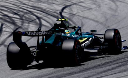 Teal and black Formula 1 car speeding on a racetrack with tire smoke trails behind it.