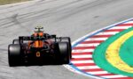 Orange Formula 1 car on a racetrack around a multicolored curb (red, white, green, yellow) during a corner.