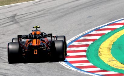 Orange Formula 1 car on a racetrack around a multicolored curb (red, white, green, yellow) during a corner.
