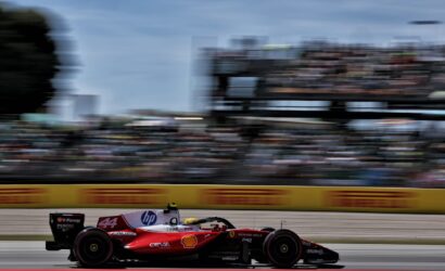 Red Formula 1 car (No. 44) speeding on a race track with blurred grandstands in the background, sponsor logos visible along the body.