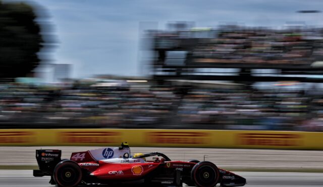 Red Formula 1 car (No. 44) speeding on a race track with blurred grandstands in the background, sponsor logos visible along the body.