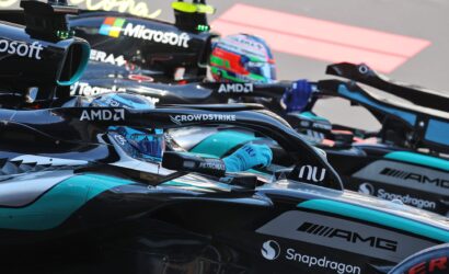 Race cars lined up in a pit area, showing sponsor logos like AMD, Microsoft, CrowdStrike and Snapdragon on glossy black and teal race bodies.
