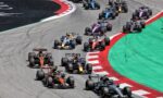 Formula 1 cars racing through a left-hand turn on a professional circuit, red-and-white curb and green runoff along the edge.