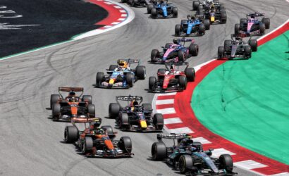 Formula 1 cars racing through a left-hand turn on a professional circuit, red-and-white curb and green runoff along the edge.