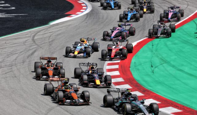 Formula 1 cars racing through a left-hand turn on a professional circuit, red-and-white curb and green runoff along the edge.