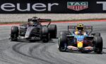 Two Formula 1 cars race side by side on a track near a wall with a TAG Heuer advertisement.