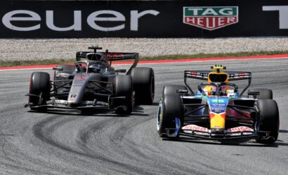 Two Formula 1 cars race side by side on a track near a wall with a TAG Heuer advertisement.