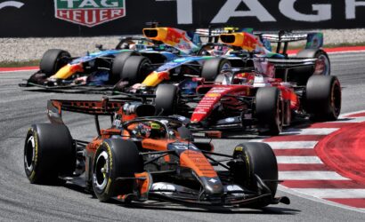Formula 1 cars race closely around a track, wheels skimming the curb with a TAG Heuer banner in the background.