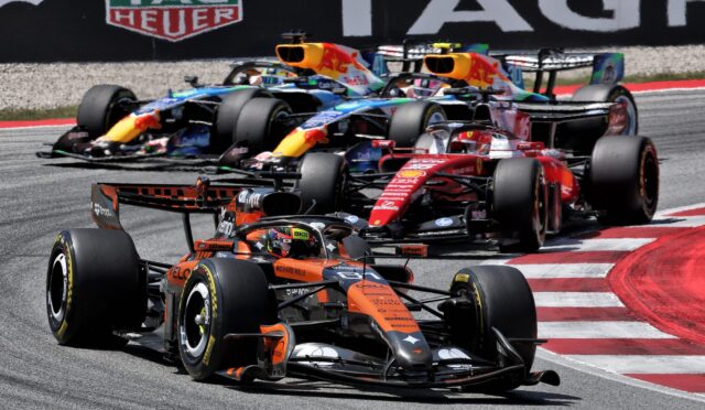 Formula 1 cars race closely around a track, wheels skimming the curb with a TAG Heuer banner in the background.